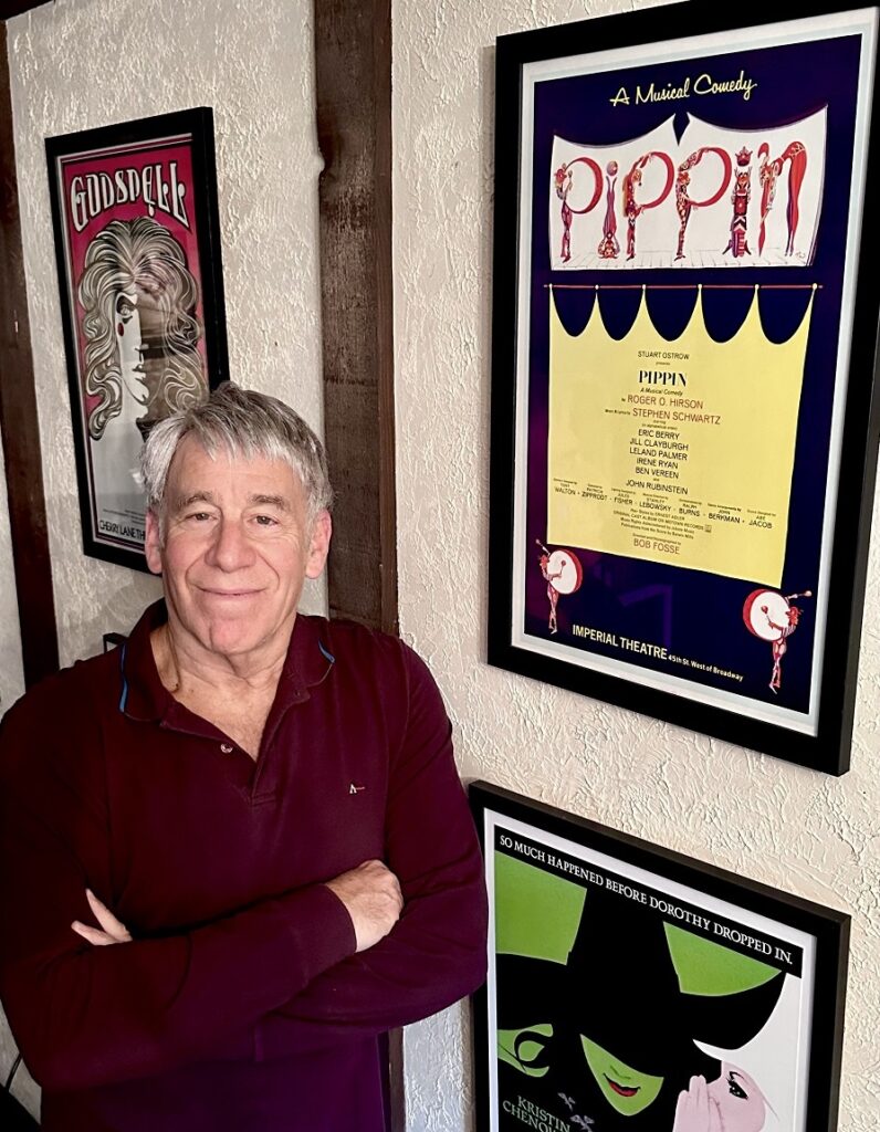 Stephen Schwartz with Broadway posters of Pippin, Wicked, and Godspell, taken October 2022. 